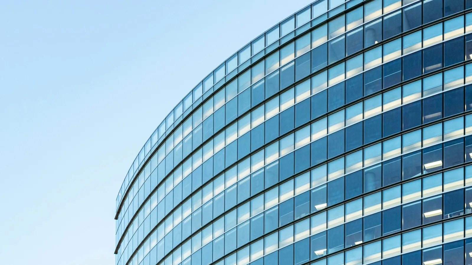 A curved glass office building against a clear sky